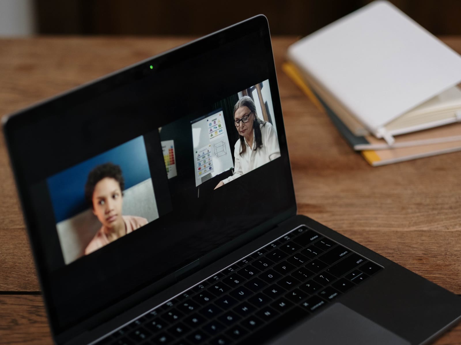 A laptop on a wooden desk showing a video call between two people